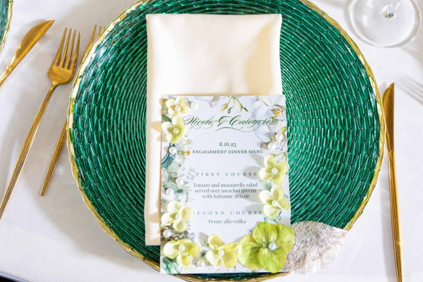 Table setting with green plates, gold cutlery, and a floral invitation card.